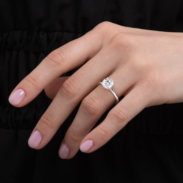 Close-up of a hand wearing a diamond ring against a black background