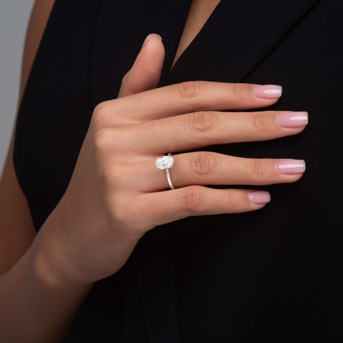 Hand wearing a diamond ring with a plain background